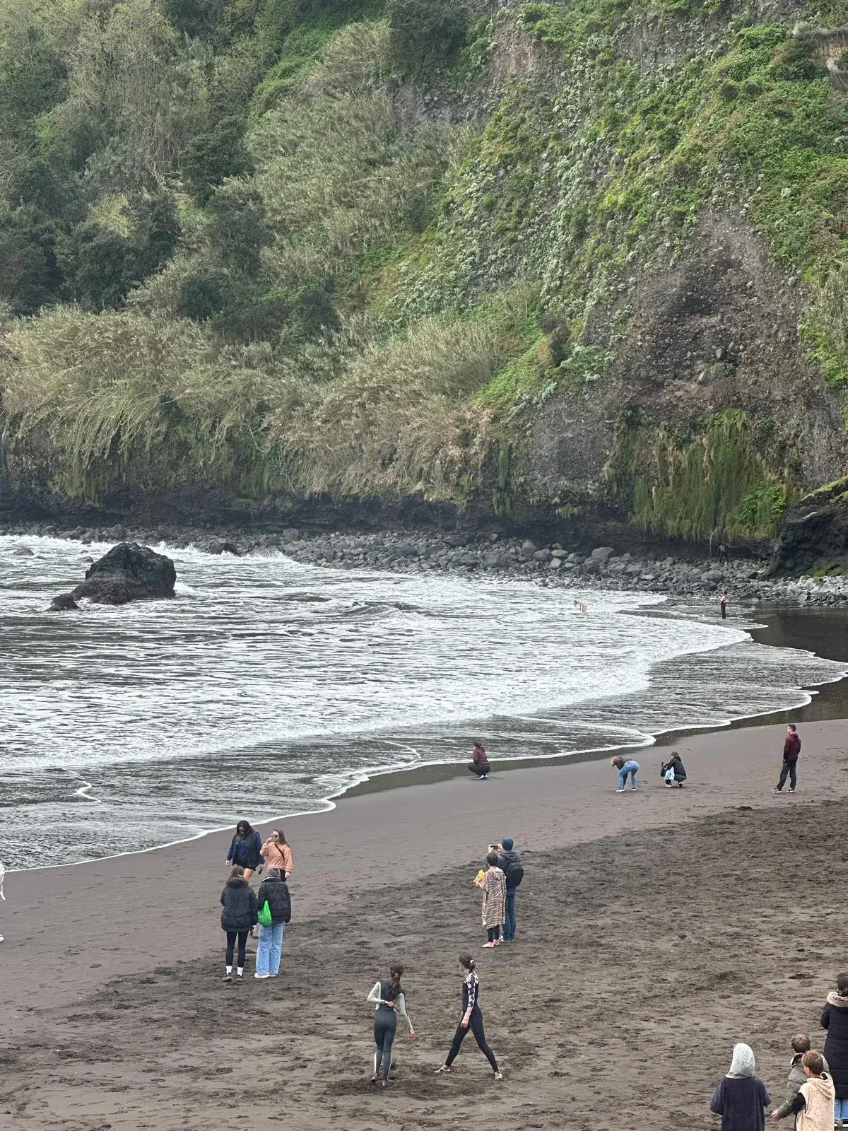 Black sand beach beneath green cliffs in Seixal