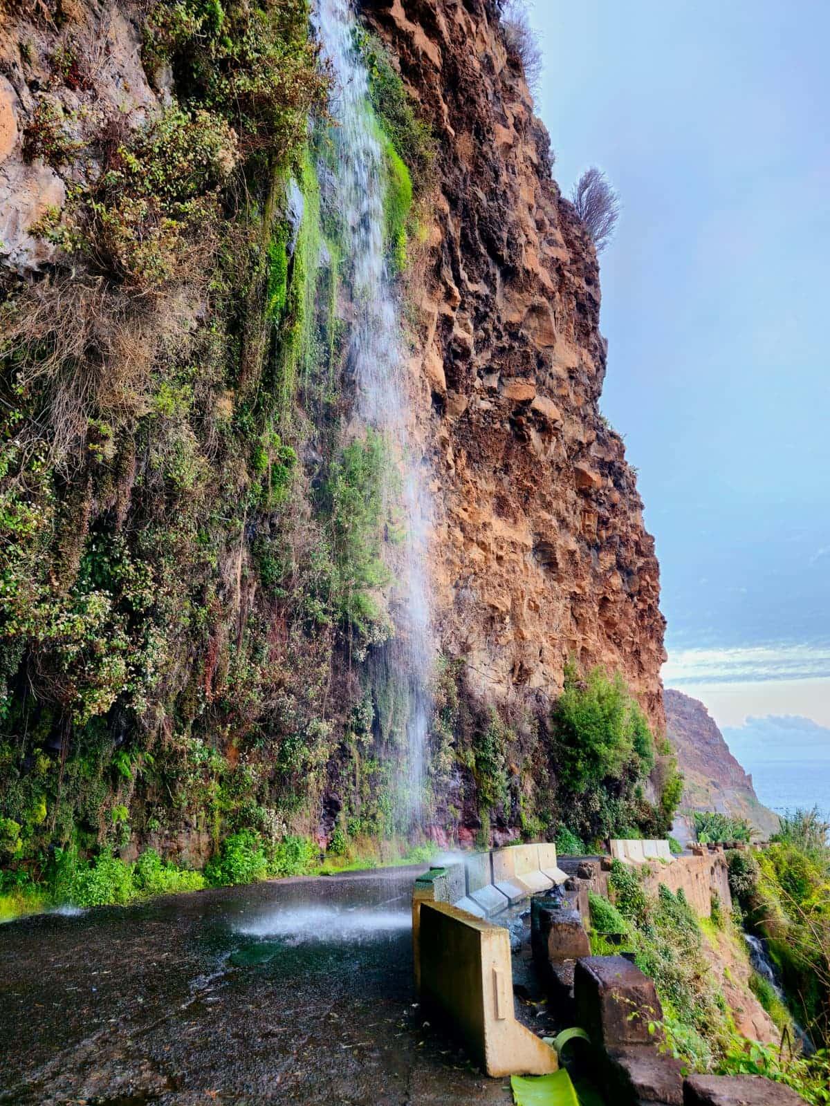 Cascata dos Anjos waterfall flowing over the coastal road in Ponta do Sol, Madeira - view 3